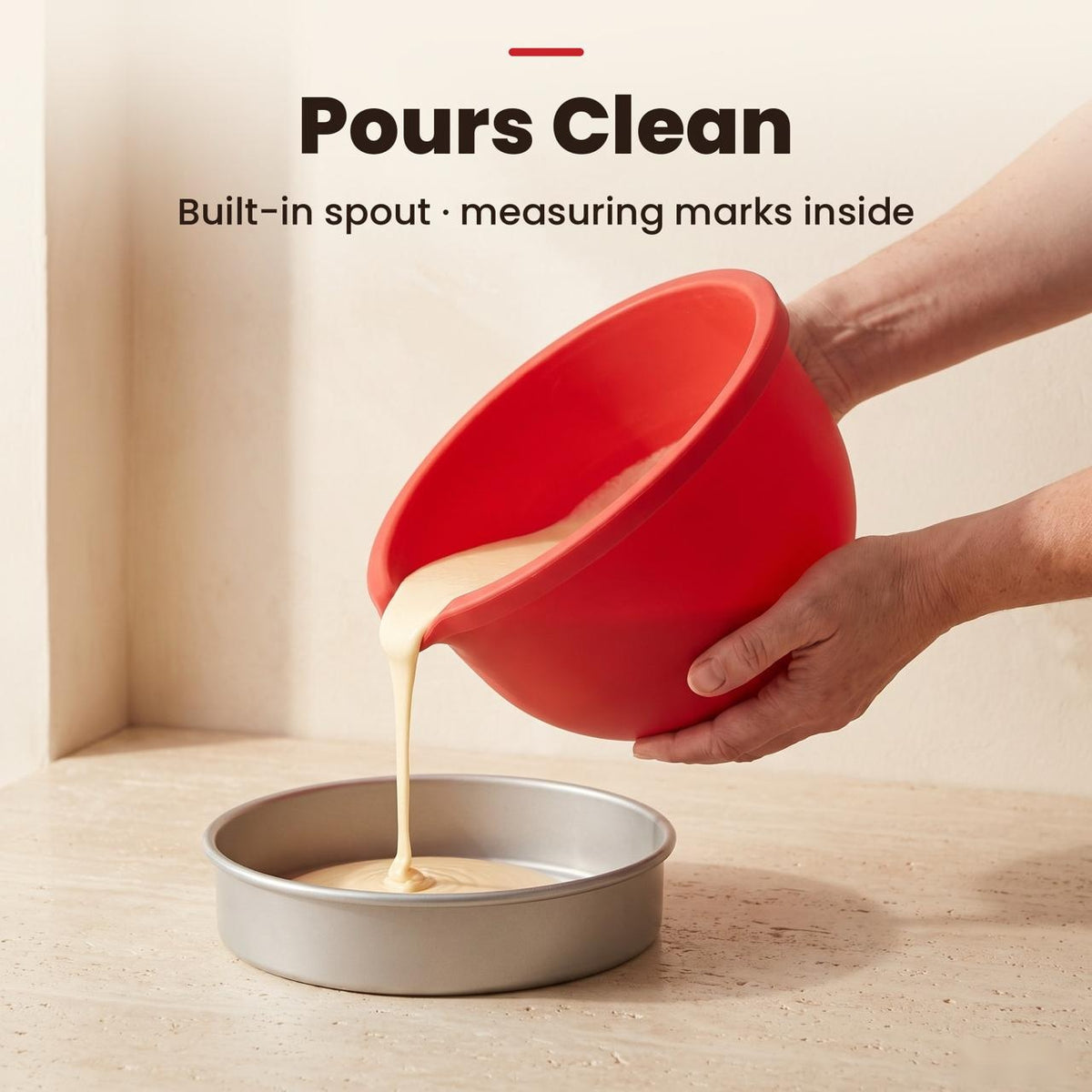 Pouring cake batter from the red silicone liner spout into a cake pan